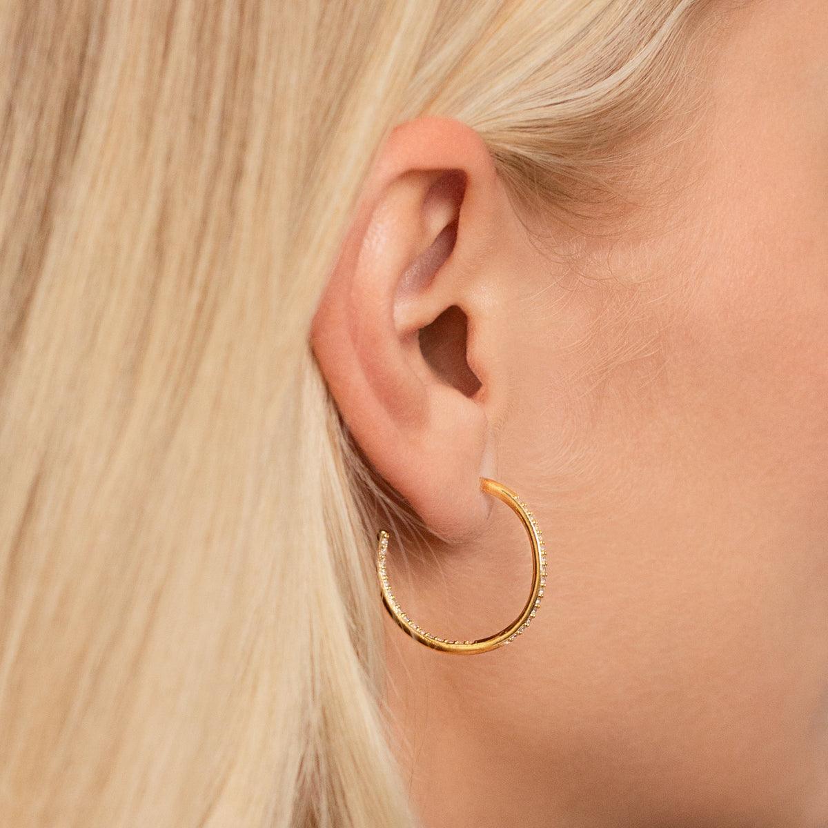 Model wearing Kylie Contemporary Crystal Hoop Earrings In Gold